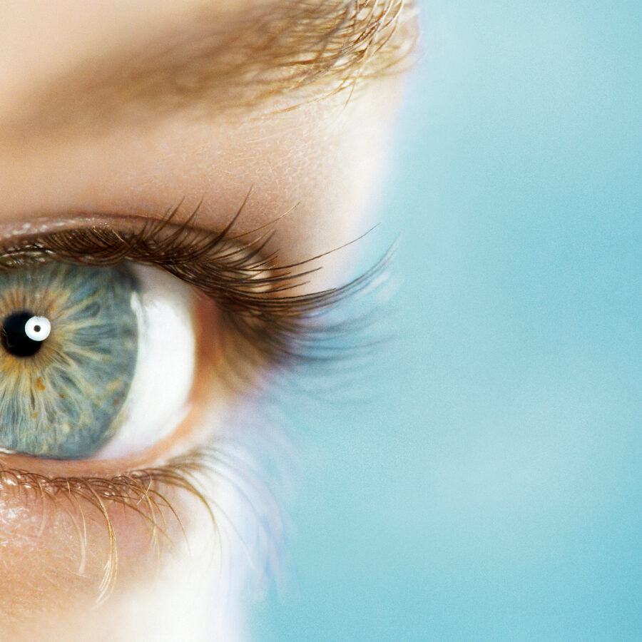 Closeup on the opened blue eye of a young woman 23 years old, blue background, empty space on right, high section, France